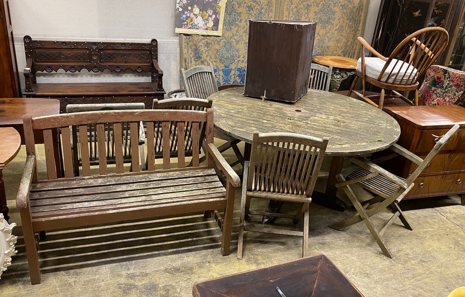 A weathered teak circular garden table, diameter 150cm, height 75cm, a matched set of six folding teak garden elbow chairs, two with arms and a teak garden bench